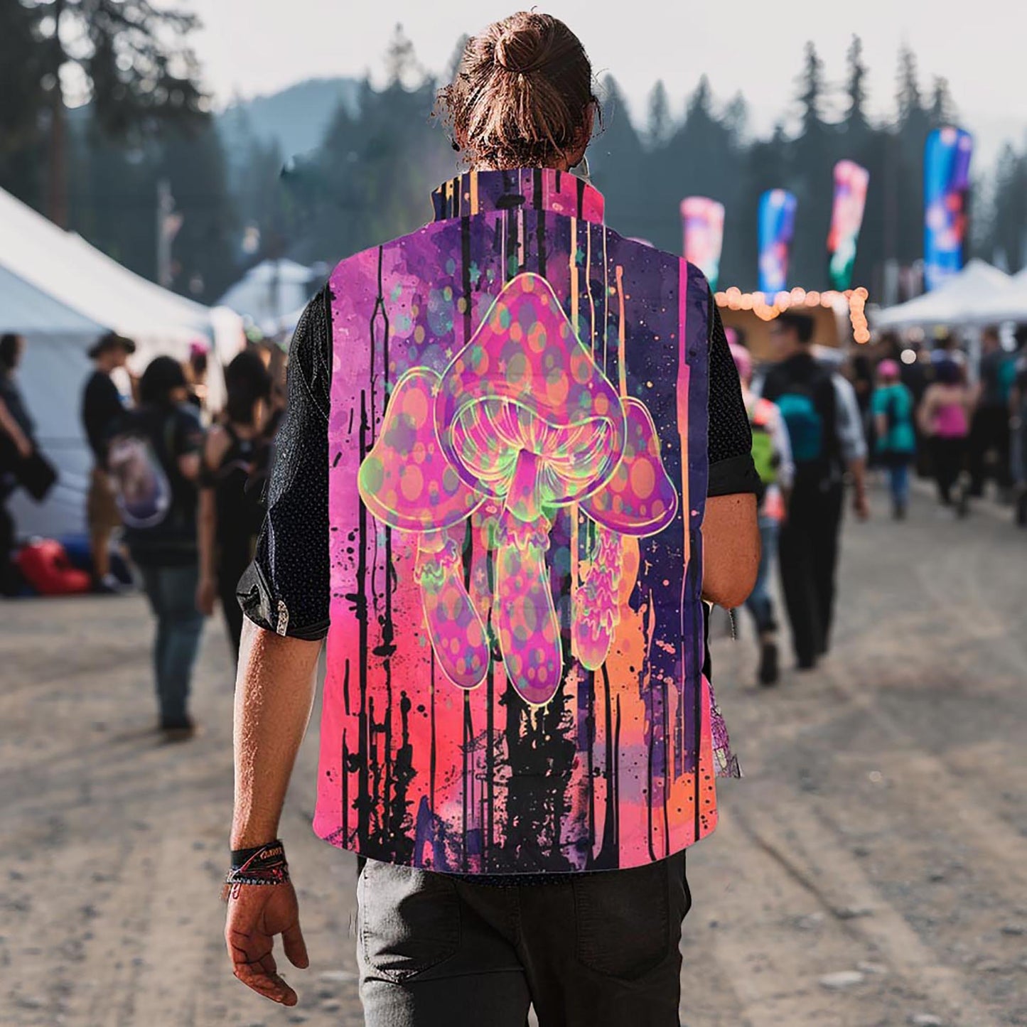 A guy in a mushroom print puffer vest, seen from behind, at Shambhala Music Festival in BC.  Shambhala Vendor Village can be seen in the background, as well as tall BC cedar trees.