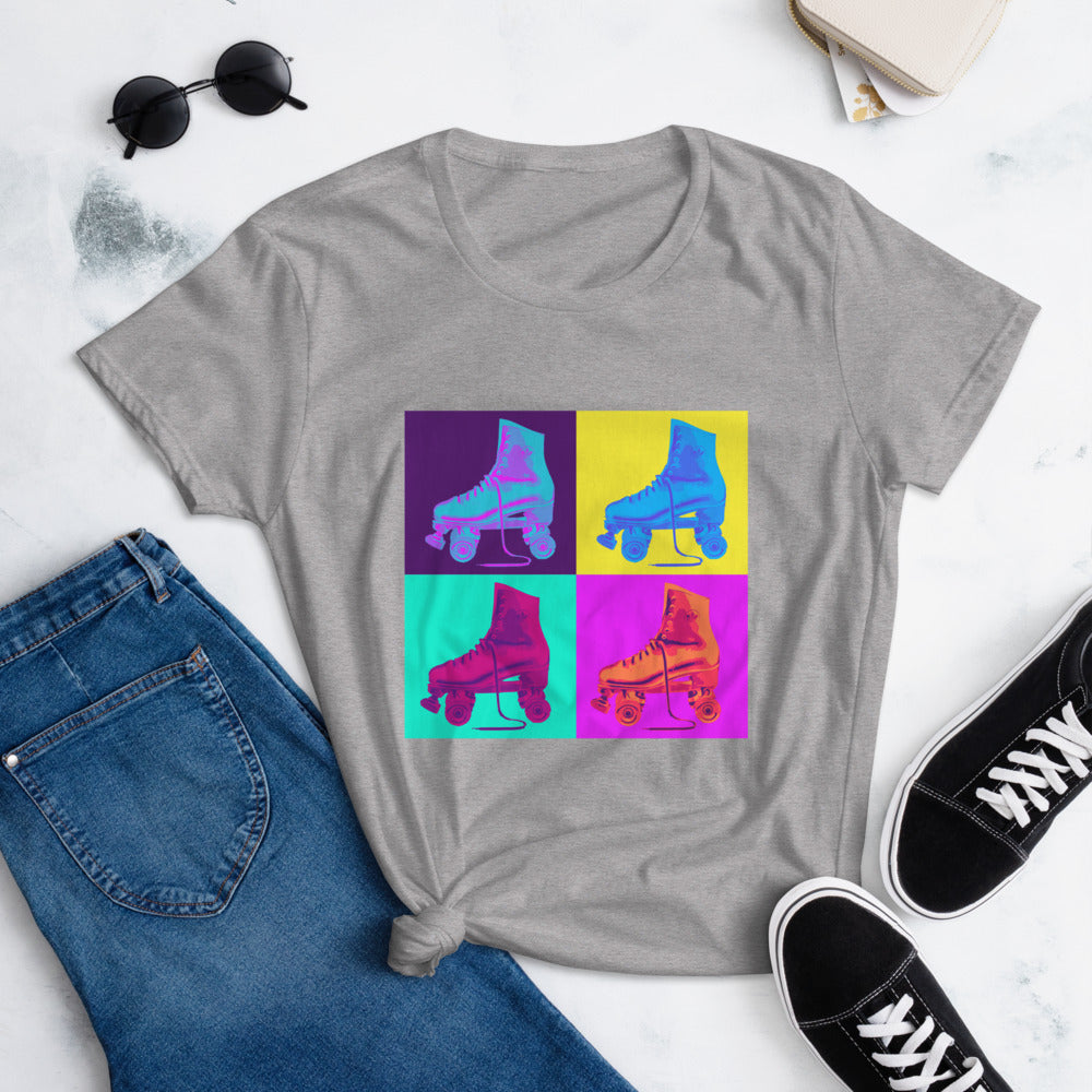 A flat photo of a heathered grey roller skate Tshirt, knotted at the side, with a print 4 brightly colored roller skates on bright coloured background squares.  The print is in a silk screen style.